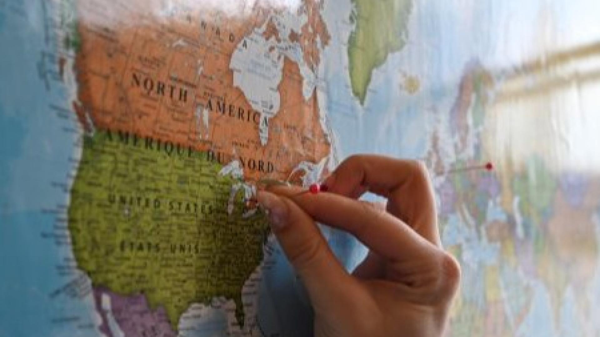 Hand placing a red pin on a map of North America.