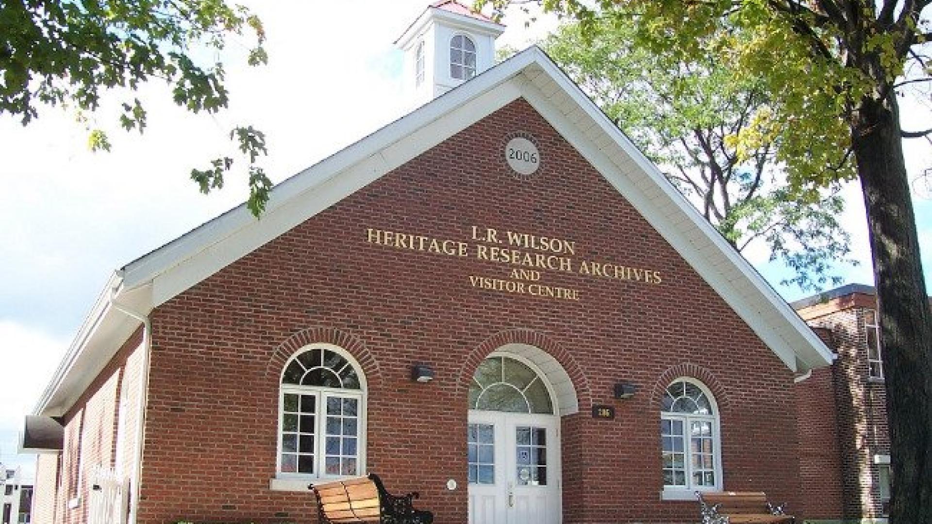 Brick building with arched windows, benches, and trees.