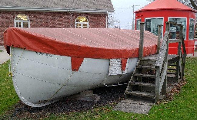 White boat with red cover and stairs, near red building.