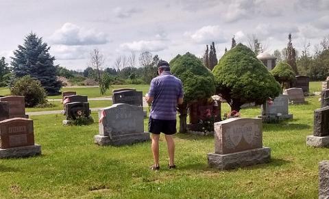 Person standing in a cemetery, surrounded by gravestones and trees.