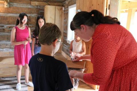 Woman in red shows craft to children in a wooden cabin.