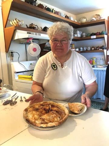Elderly woman in kitchen holding a baked pie.