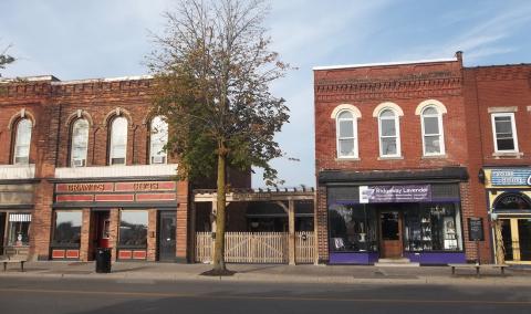 Small-town street with brick buildings and a tree in the center.