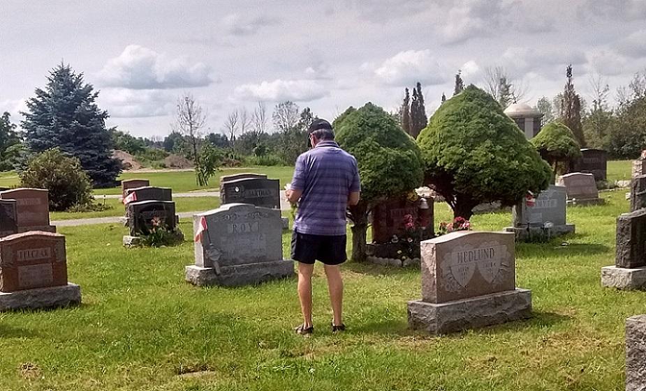 Person standing in a cemetery, surrounded by gravestones and trees.