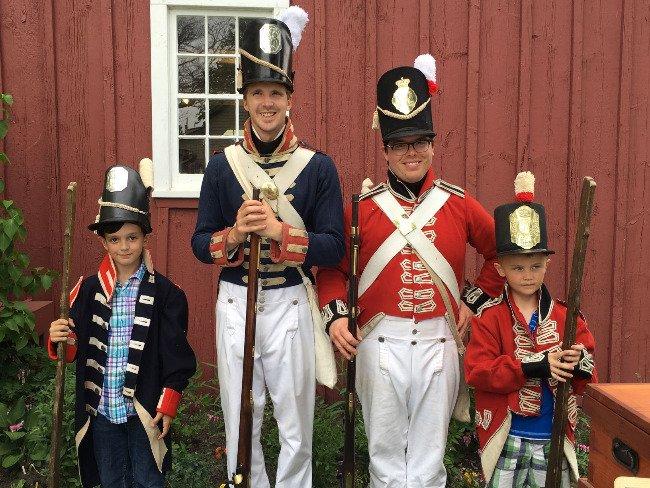 Adults and kids in historical military costumes, standing together, smiling.